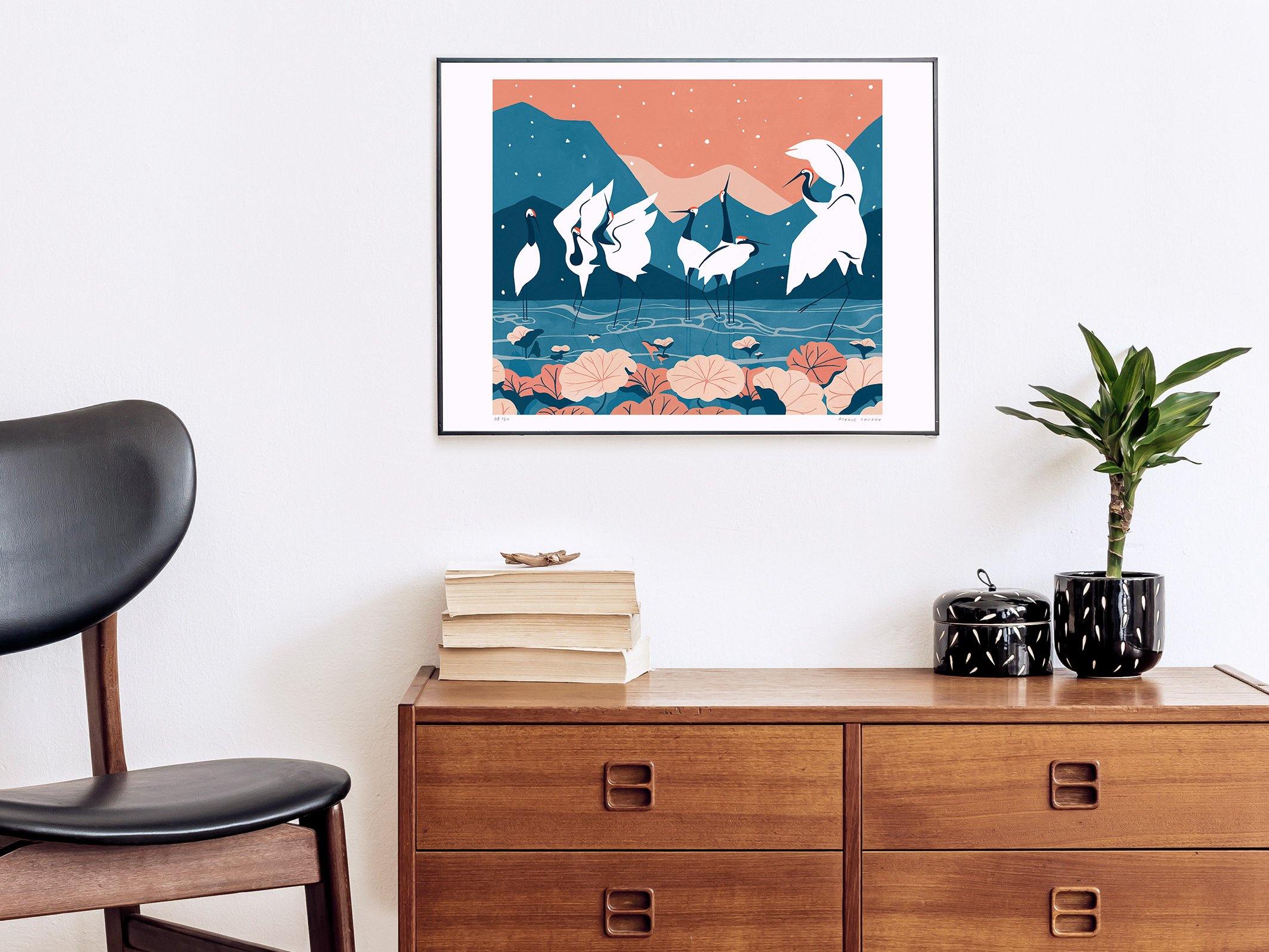 Photographie d'un salon nordique avec une affiche en tirage d'art série limité colorée bleu et corail, dessinée par Roxane Campoy illustrant des grues japonaises.